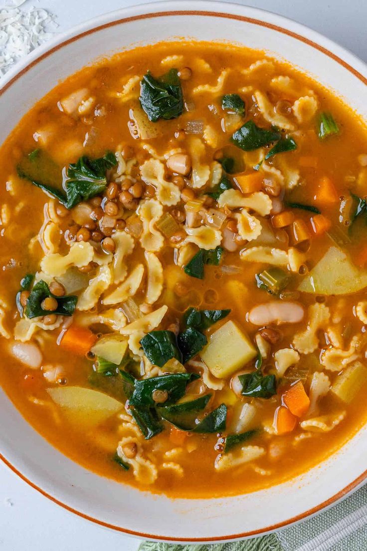 a bowl of soup with noodles, spinach and carrots on the side next to a spoon