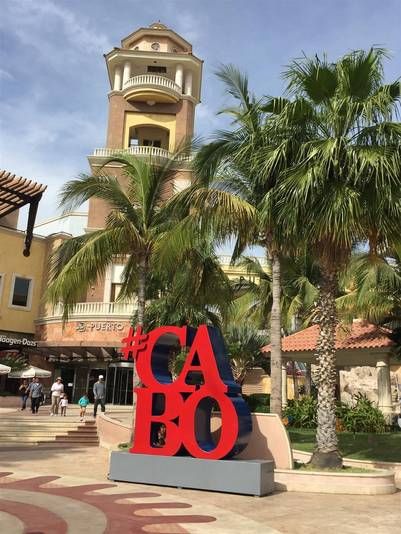 a sign that says cabo in front of some palm trees and people walking around