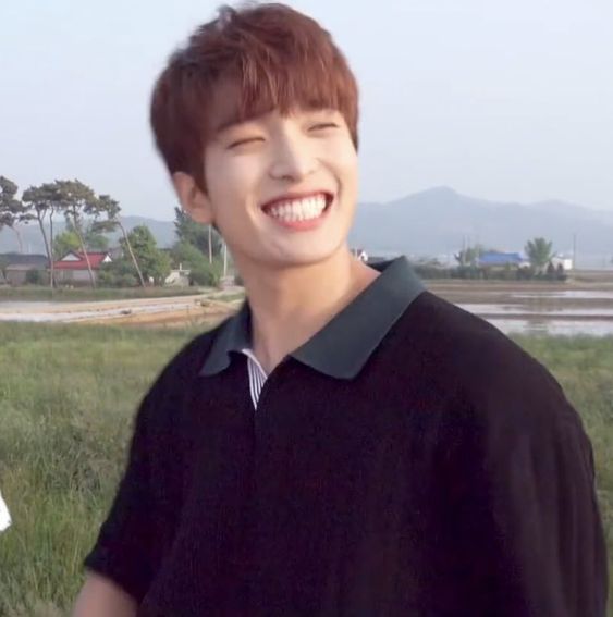 a young man standing in a field smiling at the camera