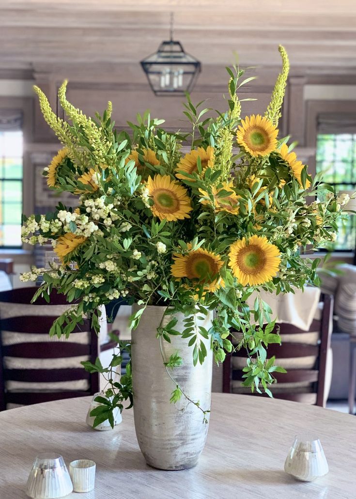 a vase filled with lots of yellow flowers on top of a table next to candles