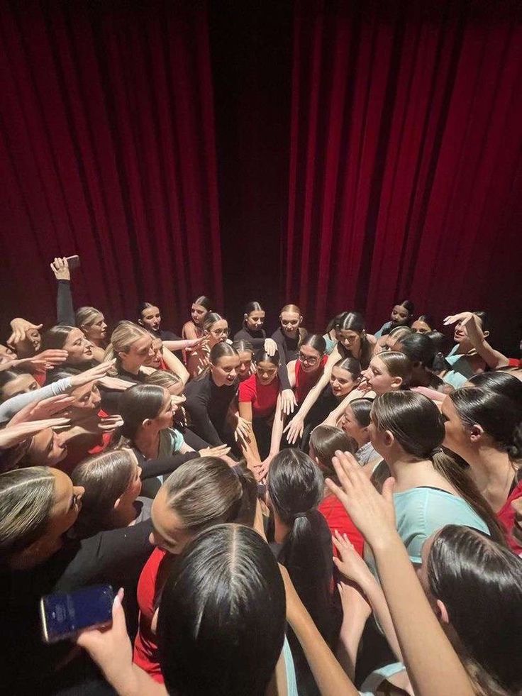 a group of people standing around each other in front of a red curtain with their hands up