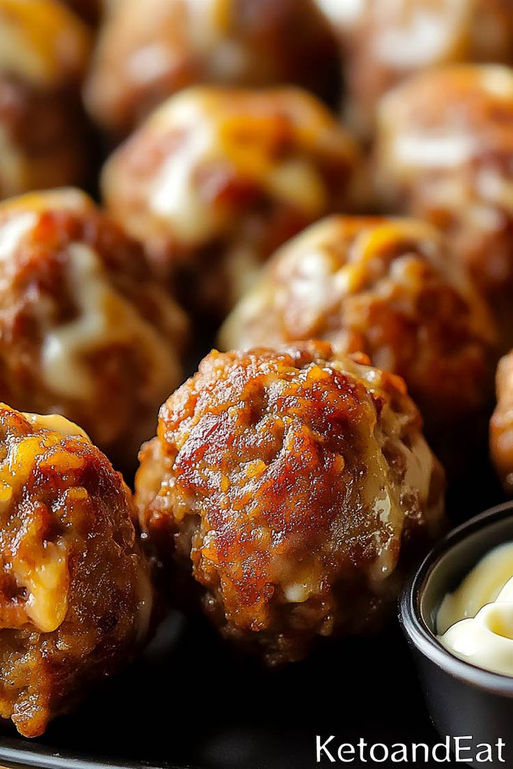 some meatballs with cheese and sauce on a black platter next to dipping sauce