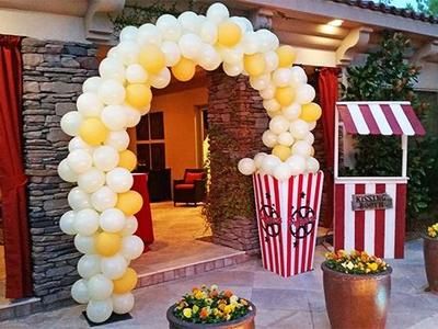 an arch made out of balloons with popcorn buckets and flowers in the foreground