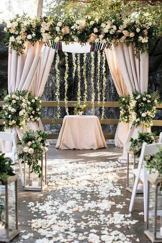 an outdoor ceremony setup with white flowers and greenery on the aisle, draped in sheer fabric