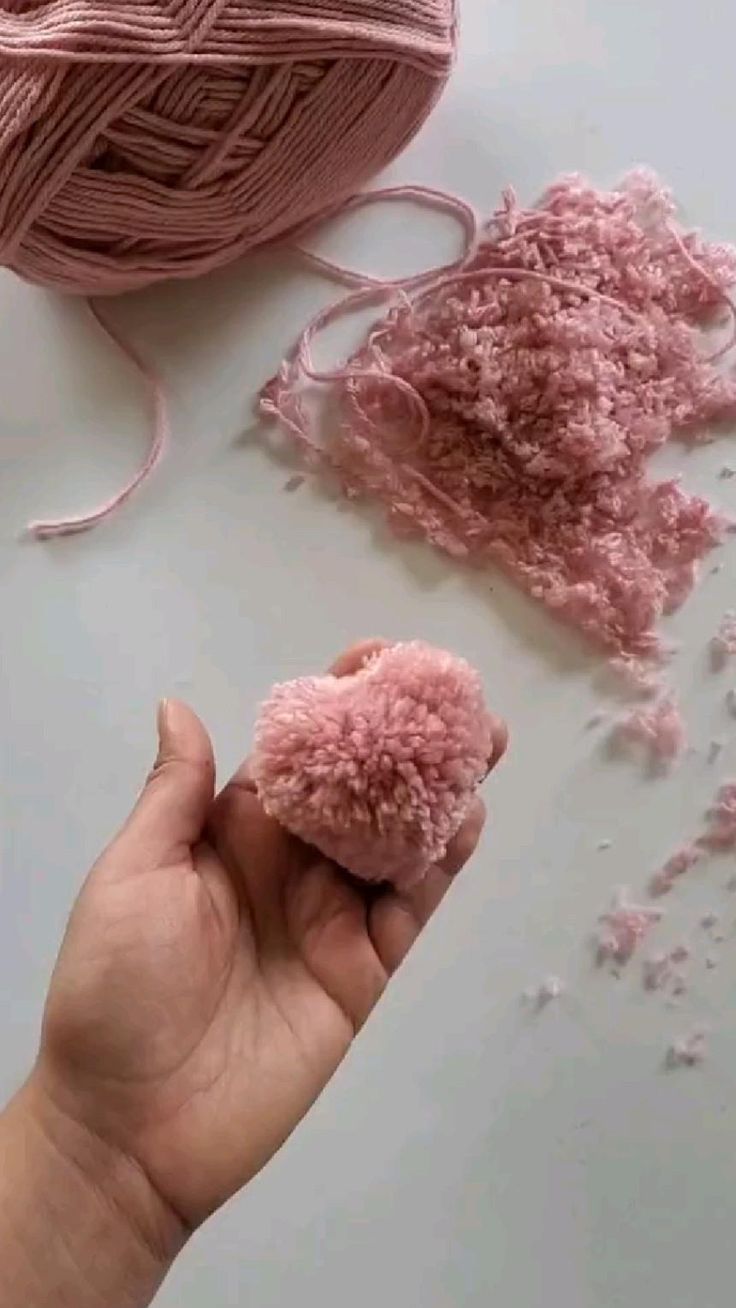 a hand holding a pink ball of yarn next to a skein of crochet