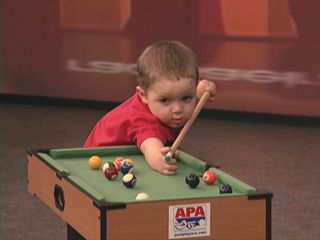 a young boy playing pool with a wooden cue and ball set in front of him