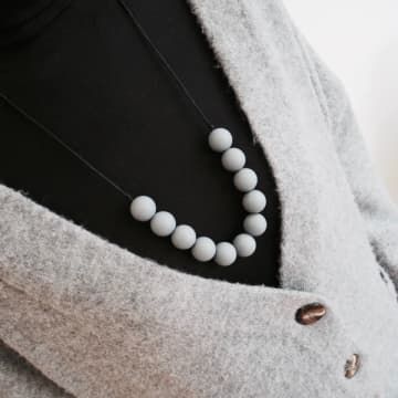 a close up of a person wearing a gray jacket and white beads on her necklace