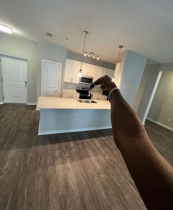 a hand pointing at an open kitchen in a new home with white cabinets and wood flooring