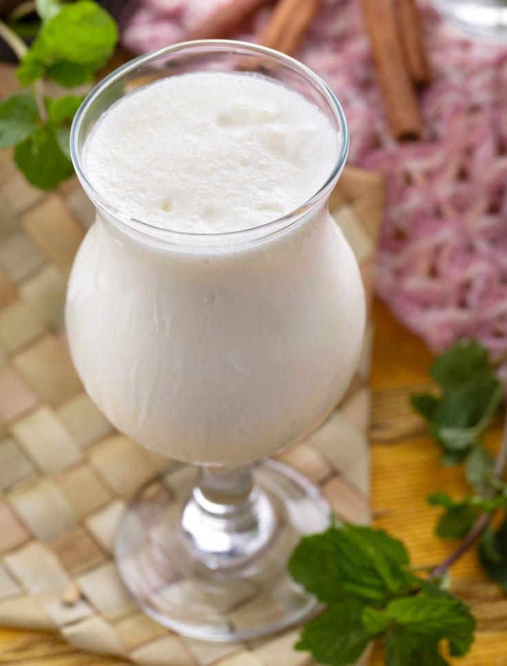 a glass filled with white liquid sitting on top of a table next to green leaves