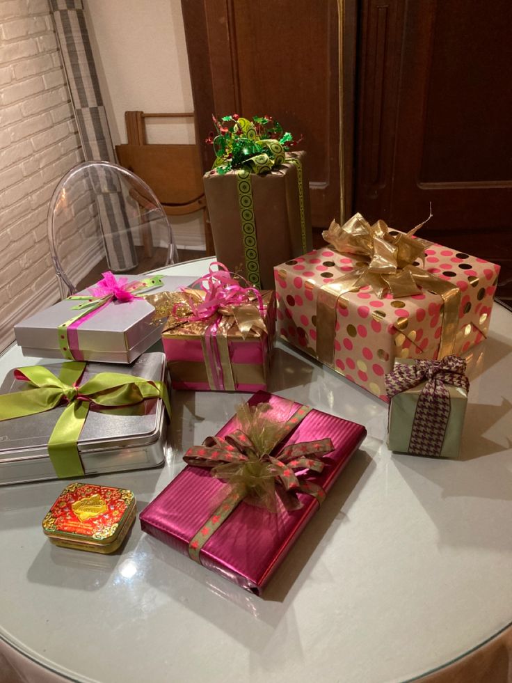 many wrapped presents are sitting on a round table with gold and pink ribbons around them