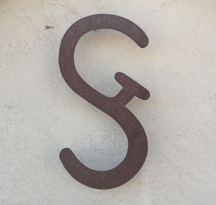 the letter s is made out of rusted metal and sits on a white wall