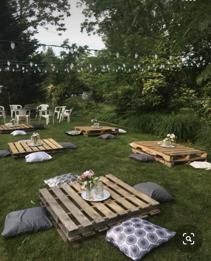 several wooden pallets are set up on the grass for an outdoor party with string lights strung above them