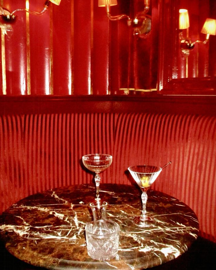 two martini glasses sitting on top of a marble table in front of a red wall