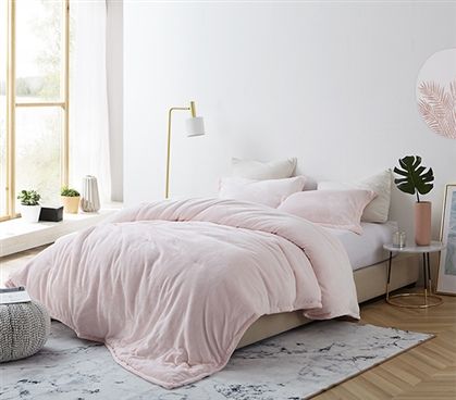 a bed with pink comforter and pillows in a white room next to a window