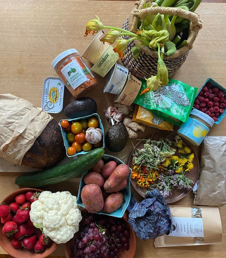 various fruits and vegetables are arranged in bowls on a wooden table with paper wrapping around them