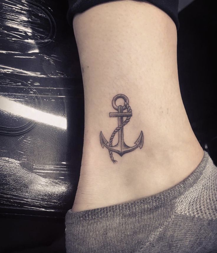 a small anchor tattoo on the side of a woman's ankle, which is black and white