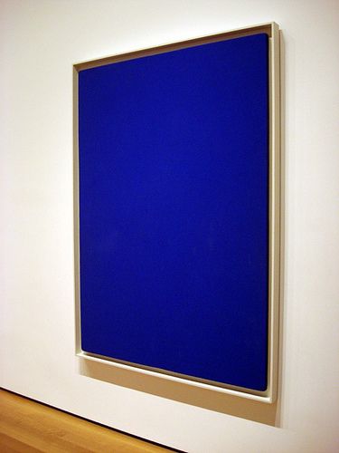 a blue painting hanging on the side of a white wall next to a wooden floor