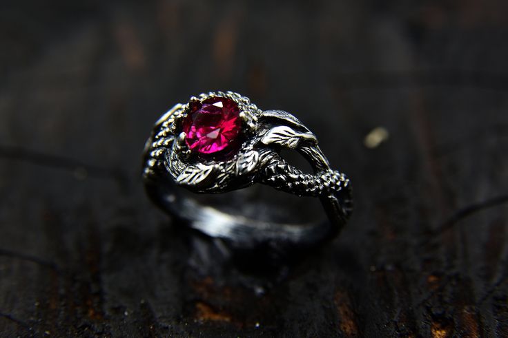 a silver ring with a pink stone in the center on a wooden surface, close up