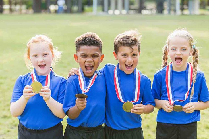 four children in blue shirts holding medals and standing next to each other with their mouths open