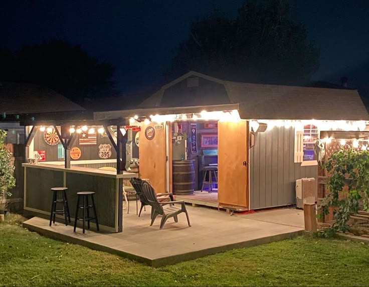 a backyard bar is lit up at night with string lights on the roof and stools