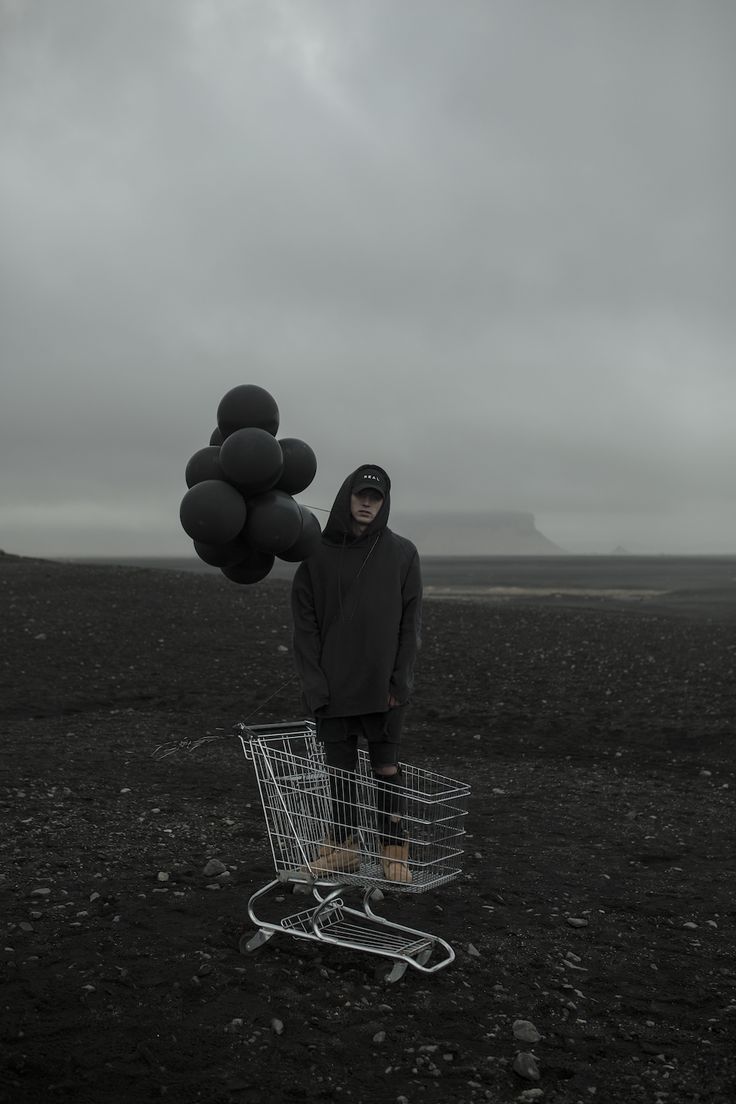 a person standing in the middle of a field with a shopping cart full of balloons