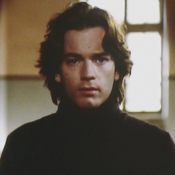 a young man with long hair wearing a black turtle neck sweater looking at the camera