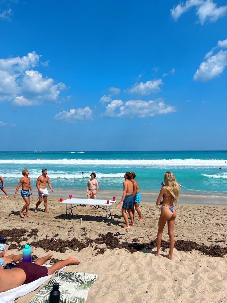 people are on the beach playing frisbee and swimming in the ocean while others watch