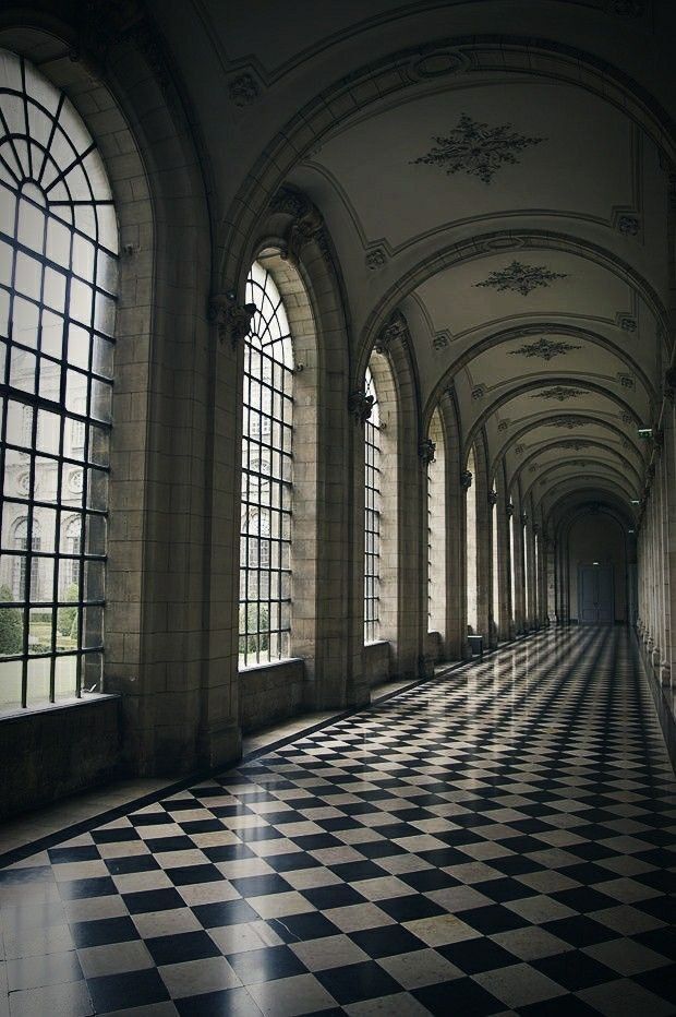 an empty hallway with large windows and black and white checkerboard flooring on both sides