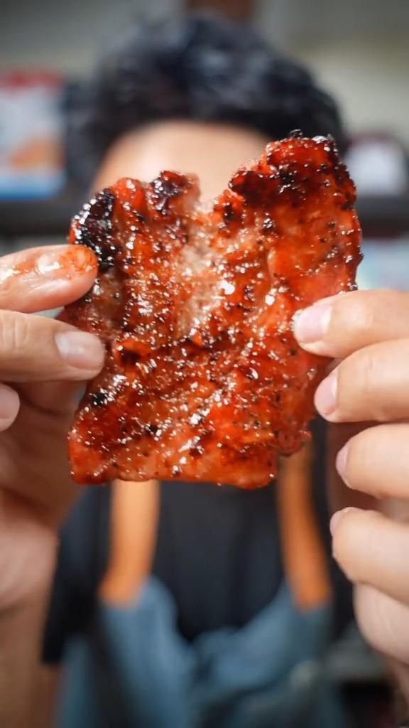 a person holding up a piece of meat in front of their face