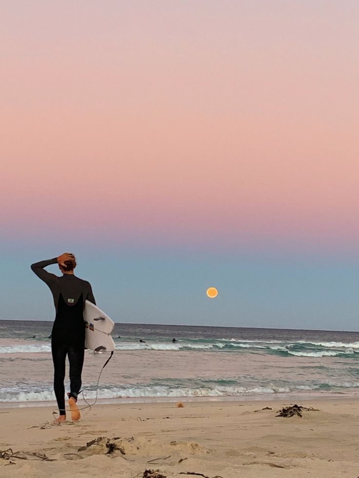 a man holding a surfboard on top of a sandy beach next to the ocean