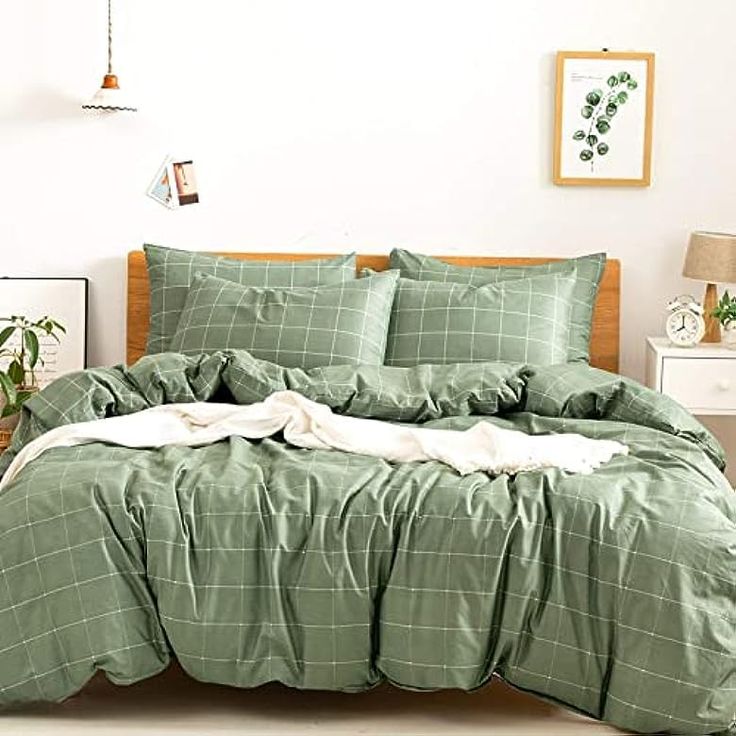 a bed with green comforter and pillows in a white room next to a plant