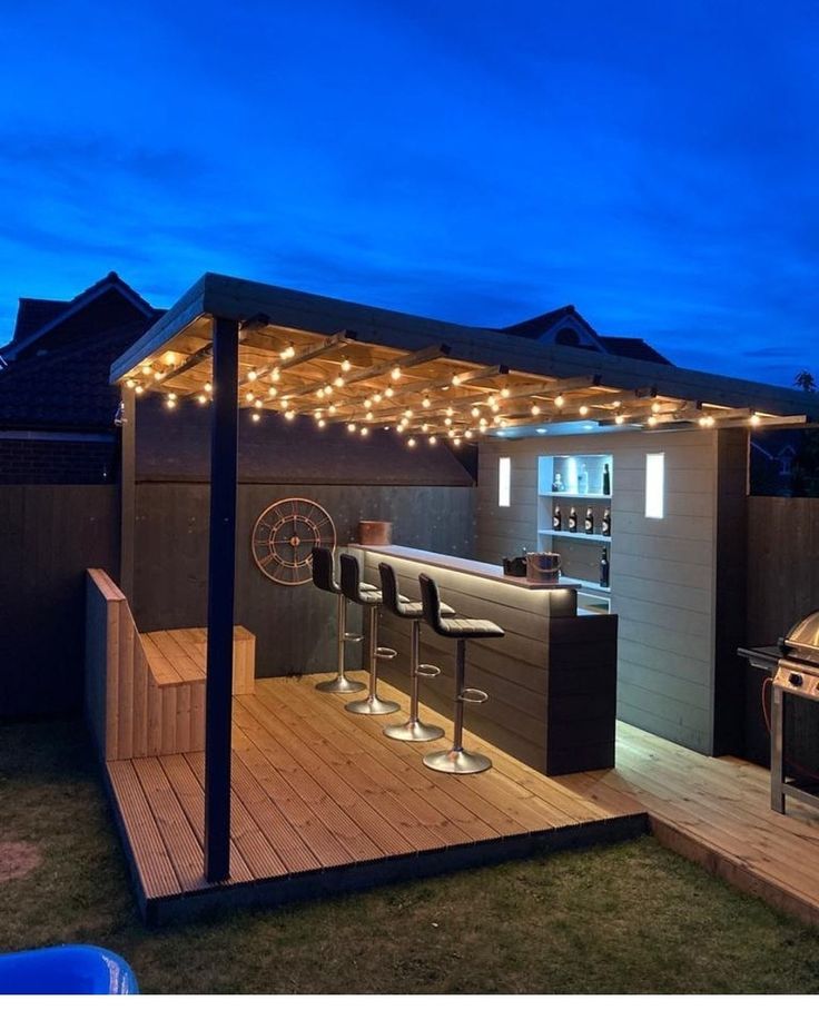 an outdoor bar with lights on the roof and barstools in the back yard