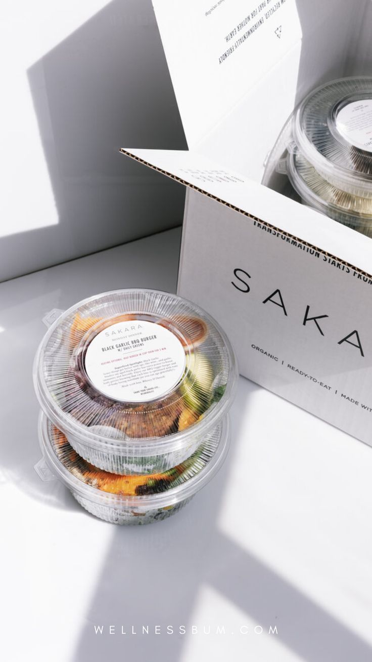 two clear plastic containers filled with food sitting on top of a white table next to a cardboard box