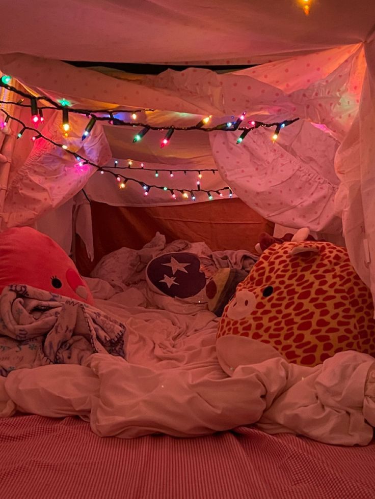 two stuffed animals sitting on top of a bed under a canopy covered in blankets and lights