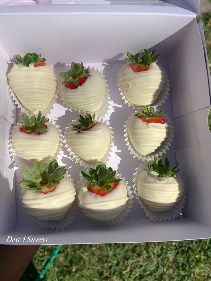 a box filled with white chocolate covered strawberries on top of green leaves and grass