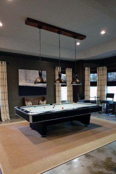 a pool table in the middle of a living room with two lamps hanging over it