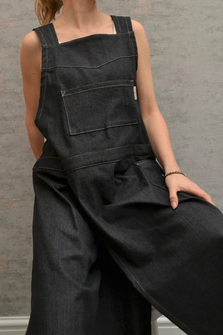 a woman standing in front of a wall with her hands on her hips and wearing black overalls