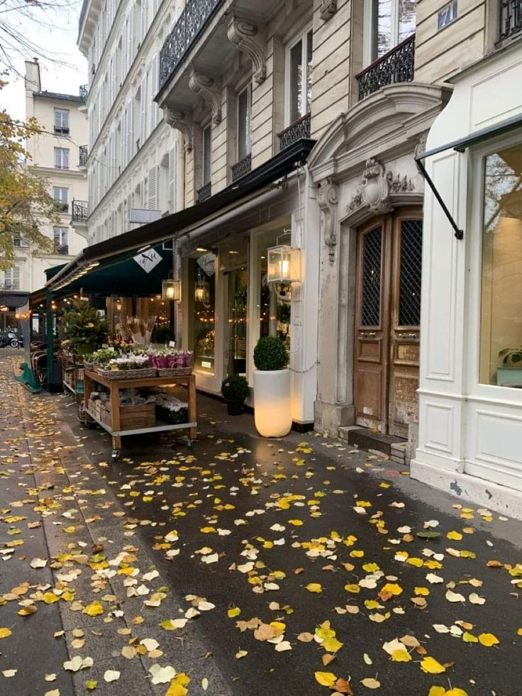 an empty street with lots of leaves on the ground and tables in front of it