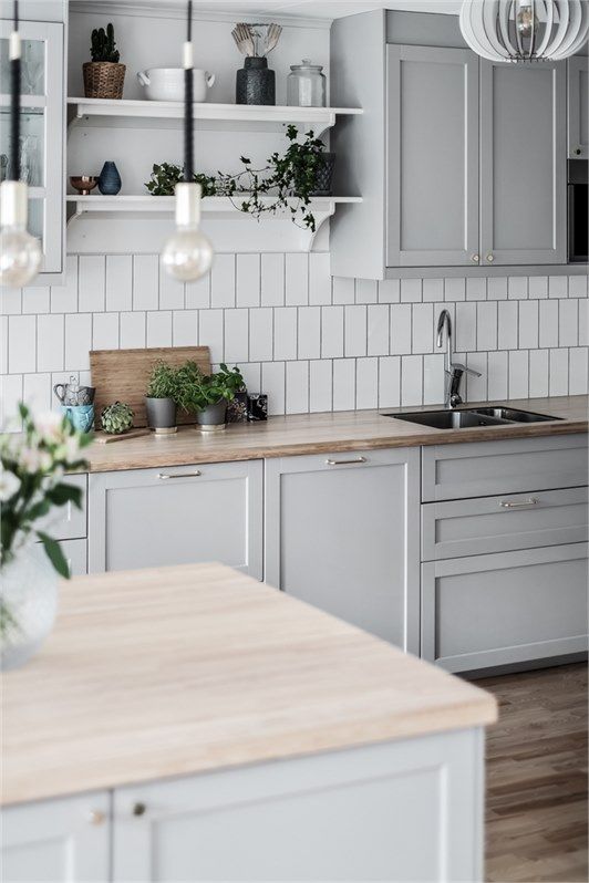 a kitchen with gray cabinets and white subway tile backsplash, wood countertops