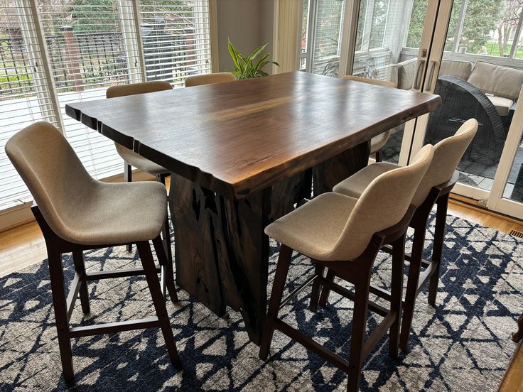 a dining room table with four chairs and a rug on the floor in front of it