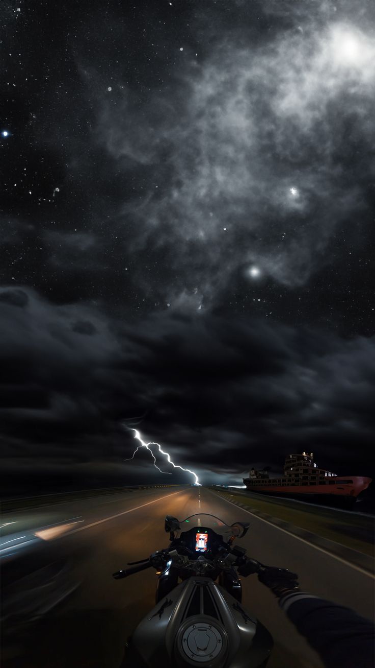 a motorcycle is driving down the road at night with lightning in the sky behind it