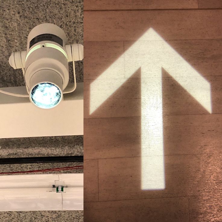 a white arrow is projected on the floor next to a camera and light fixture in an office building