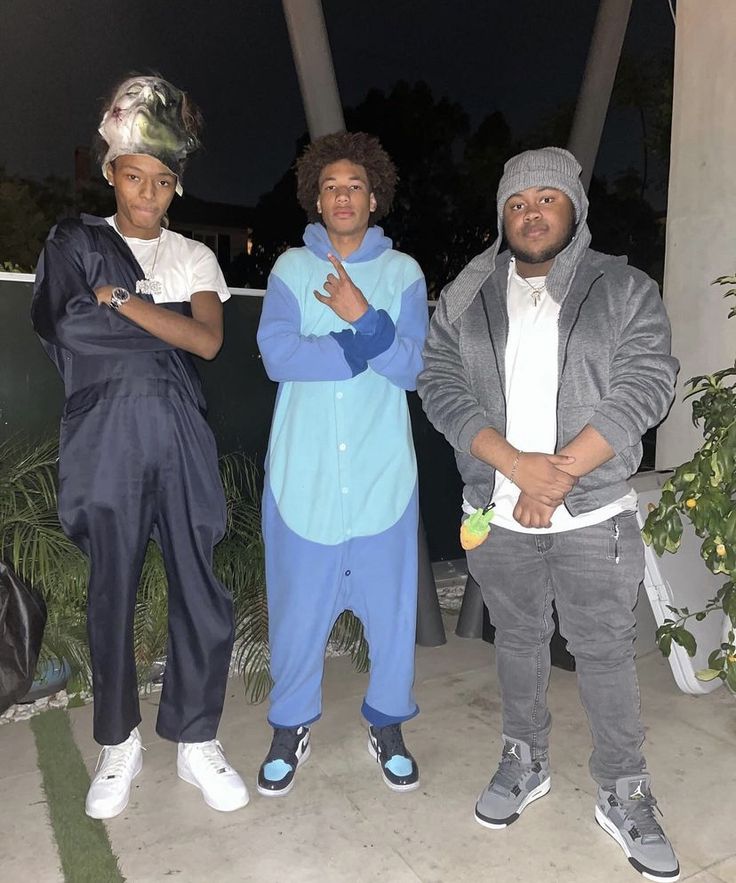 three young men standing next to each other in front of a house at night with palm trees