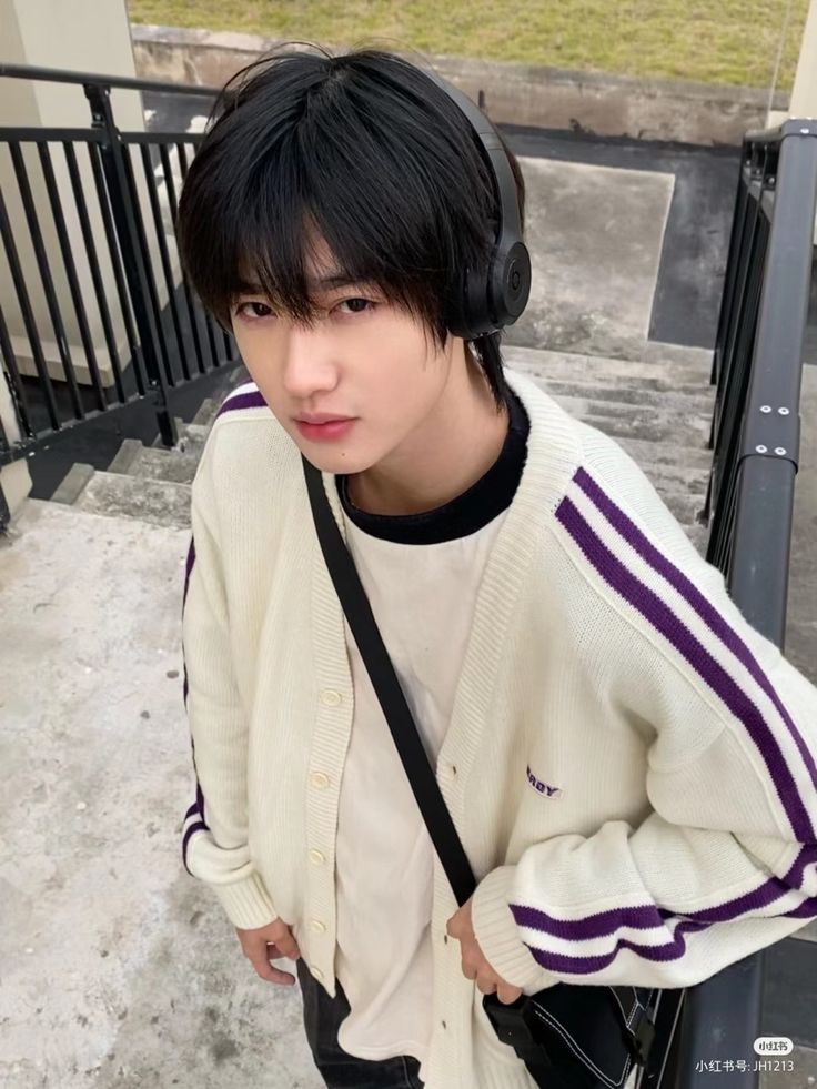 a young man with headphones on standing next to a stair case and looking at the camera