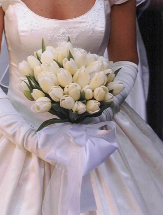 a bride holding a bouquet of white tulips in her hand and wearing a wedding dress