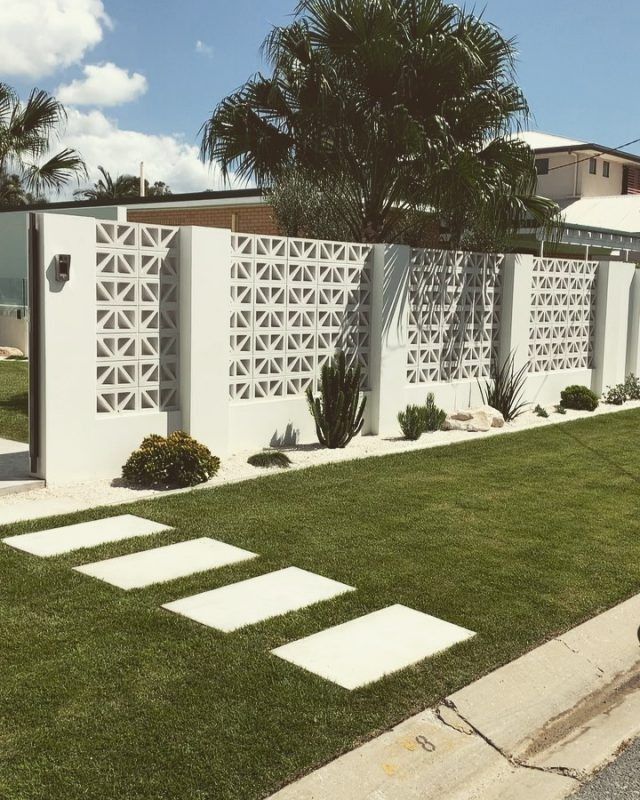 a white fence and grass area in front of a house with palm trees on the other side