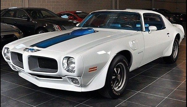 a white pontiac car parked in a garage next to other cars and one has a blue stripe on the hood