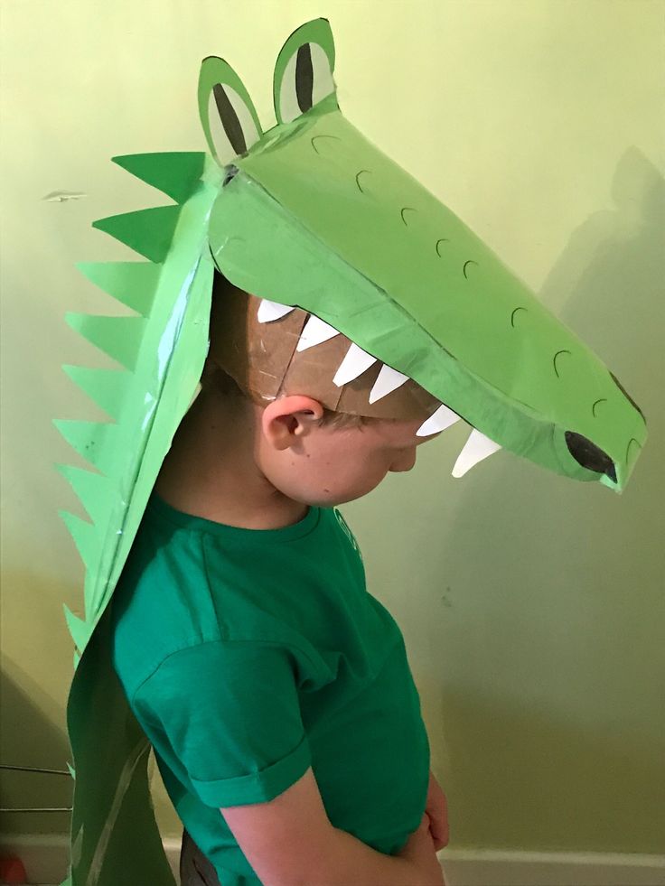 a young boy wearing a green paper hat with a large alligator's head on it