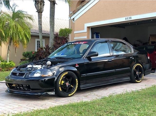 a black car with yellow rims parked in front of a house next to a red fire hydrant