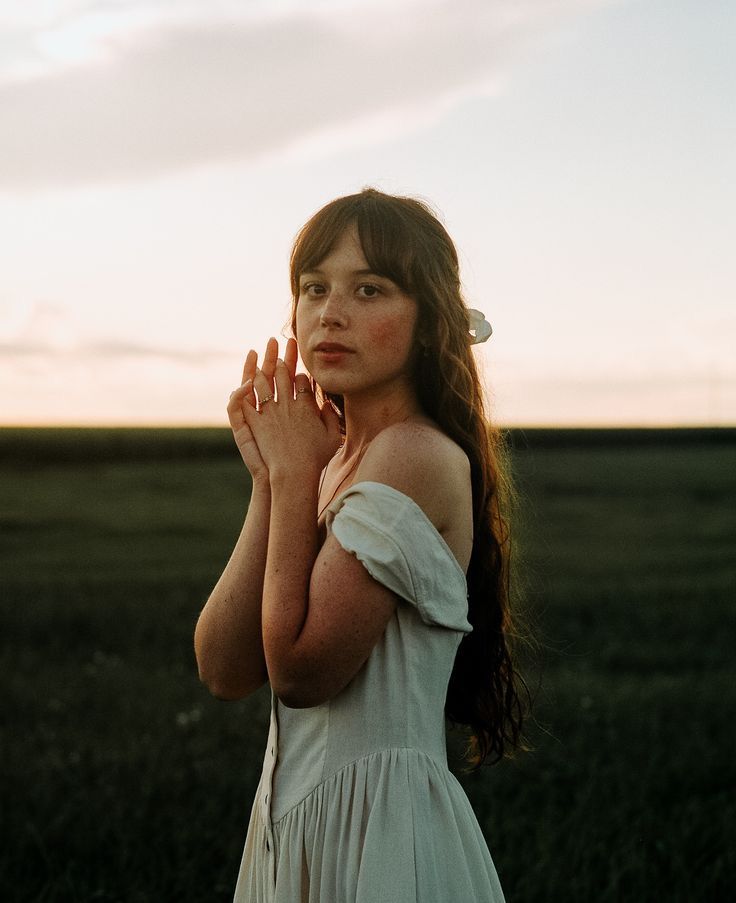 a woman standing in a field with her hands together